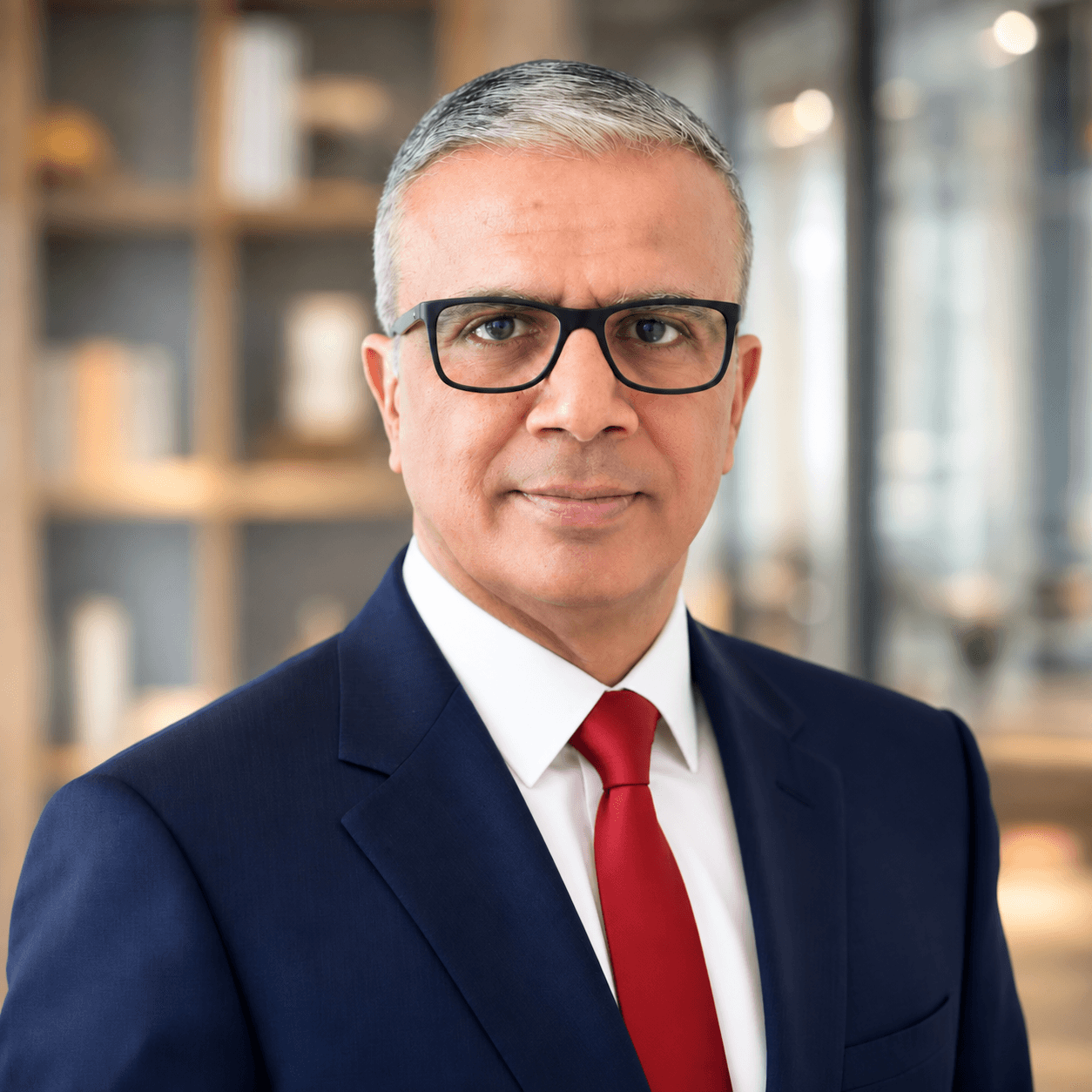 Middle-aged man with graying hair and glasses wearing a navy suit and red tie.